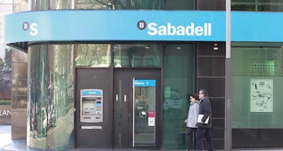 Dos personas andando delante de una oficina de Banco Sabadell