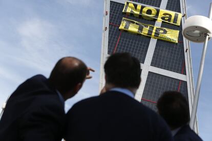 Varias personas contemplan los dos carteles colocados por los activistas de Greenpeace en una de las Torres Kio de Madrid.