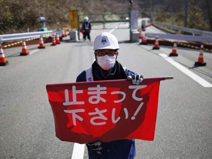 Un guarda de seguridad sostiene una bandera que dice "¡Pare!" en un puesto de control de Fukushima.