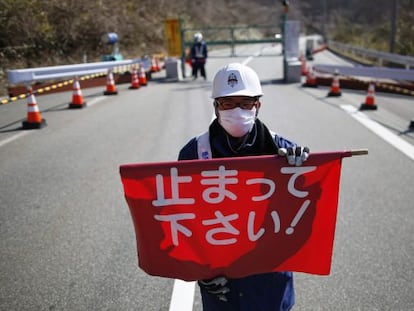 Un guarda de seguridad sostiene una bandera que dice "¡Pare!" en un puesto de control de Fukushima.