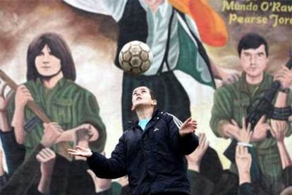 Un chico juega con un balón frente a un mural del IRA en Belfast.