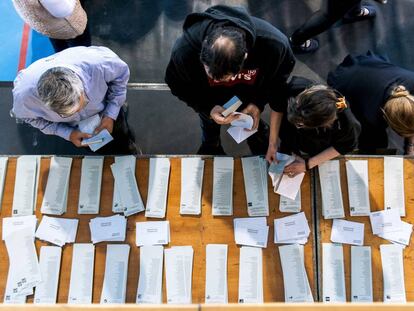 Electores en mesa de papeletas y sobres en un colegio electoral.