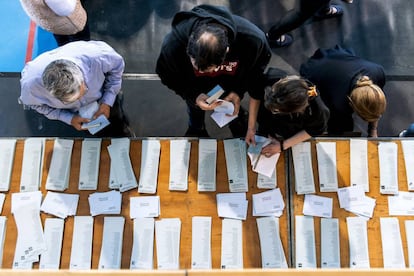 Electores en mesa de papeletas y sobres en un colegio electoral.