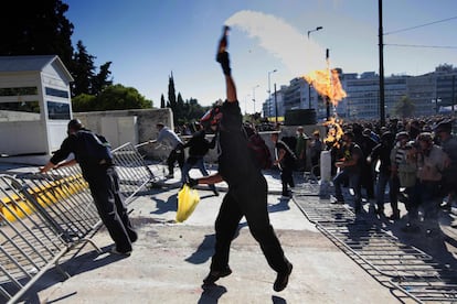 Un manifestante enmascarado lanza un artefacto contra efectivos antidisturbios durante la protesta en Atenas.