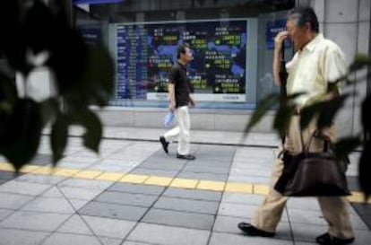 Varios viandantes pasan delante de un escaparate que exhibe una pantalla con información bursátil.. El índice Nikkei de la Bolsa de Tokio abrió hoy con una bajada del 0,40 por ciento. EFE/Archivo