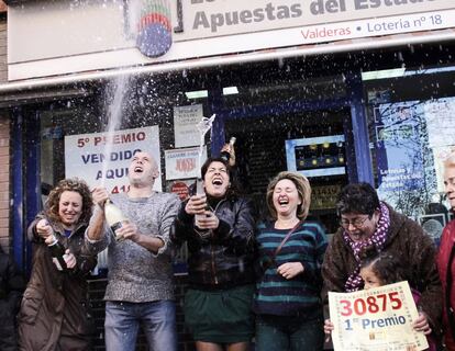 Algunos de los agraciados con el primer premio de la lotería del Niño, con el 30.875, en Alcorcón (Madrid), lo celebran con cava a la puerta de la administración de loterías.