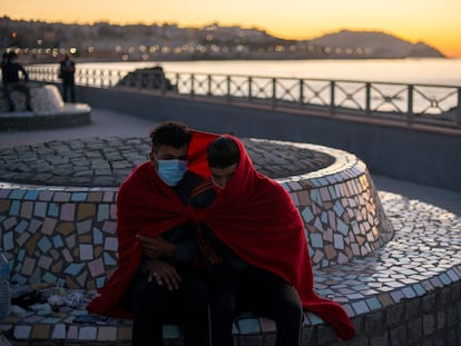 Dos jóvenes inmigrantes se protegen del frío a primera hora de la mañana del 19 de mayo cerca de la playa ceutí de El Tarajal.