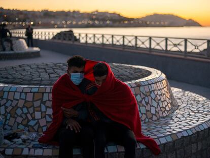 Dos jóvenes inmigrantes se protegen del frío a primera hora de la mañana cerca de la playa ceutí de El Tarajal.