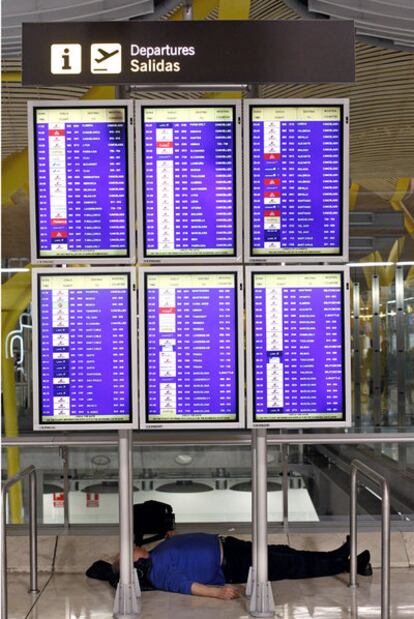 Un hombre tumbado detrás de los paneles de salidas de la T-4 del aeropuerto de Barajas (Madrid).