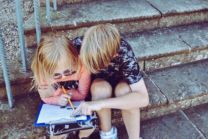 Dos niños repasan la tarea, sentados en una escalera.