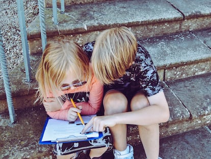 Dos niños repasan la tarea, sentados en una escalera.