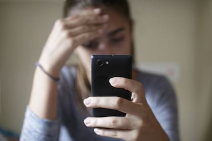 Uma adolescente cabisbaixa depois de receber uma ameaça por meio de seu celular.