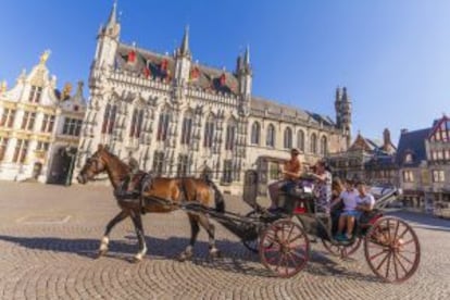 Turistas en un coche de caballos en el Burg, la playa del Ayuntamiento, en Brujas.