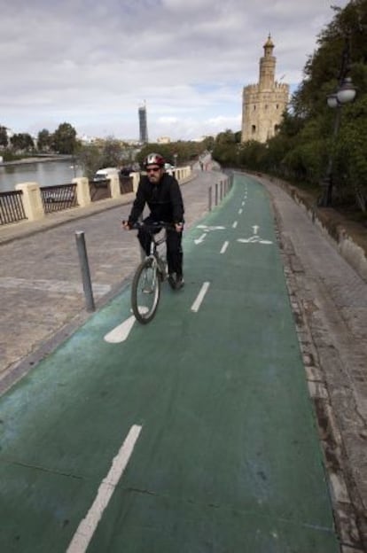 Un hombre pedalea frente a la Torre del Oro por el carril bici de Sevilla.