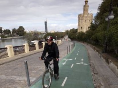 Un hombre pedalea frente a la Torre del Oro por el carril bici de Sevilla.