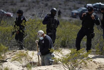 Policías federales protegen el trabajo de un forense en una fosa común.