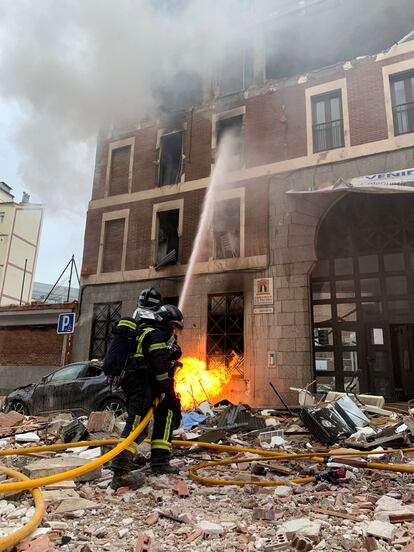 Dos bomberos apagan el fuego que salía del edificio de la explosión.