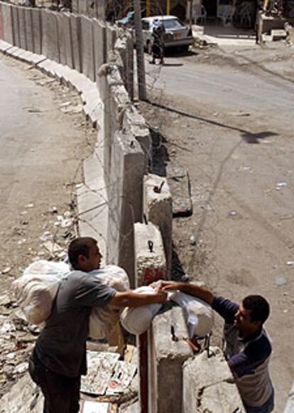 Un palestino entrega a otro por encima del muro unas bolsas de pan.