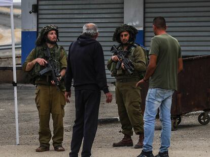 Dos soldados israelíes y dos palestinos, en la carretera principal de la localidad cisjordana de Huwara, el pasado noviembre.