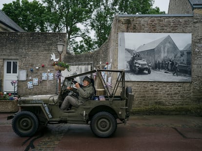 Un hombre conduce un antiguo coche militar junto a una fotografía de la entrada de las tropas aliadas en el pueblo de Colleville-sur-mer.