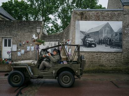 Un hombre conduce un antiguo coche militar junto a una fotografía de la entrada de las tropas aliadas en el pueblo de Colleville-sur-mer.