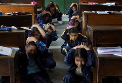Estudiantes nepalíes se protegen bajo sus pupitres durante un simulacro de terremoto con motivo del 4 aniversario del devastador seísmo que sufrió el país hace cuatro años, este jueves en Lalitpur (Nepal). 