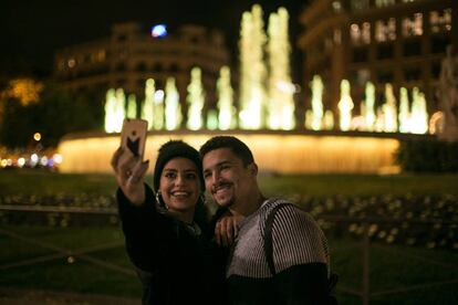 Una pareja se fotograf&iacute;a ante las fuentes gemelas de Plaza Catalu&ntilde;a, en Barcelona, iluminadas de amarillo en solidaridad con los presos.