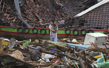Un hombre con un niño en brazos obseva los daños en una aldea devastada por el tsunami en Sumur, Indonesia.