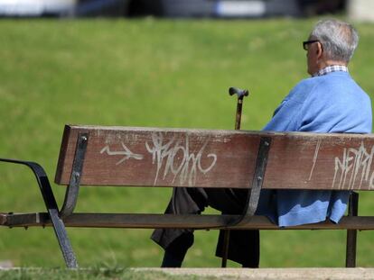Un jubilado sentado con su bast&oacute;n en un banco de un parque.