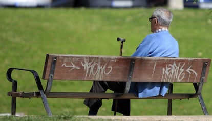 Un jubilado sentado con su bast&oacute;n en un banco de un parque.