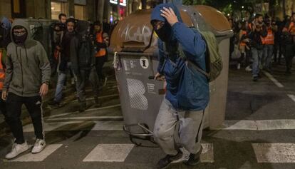 Un encapuchado arrastra un contenedor en Barcelona.