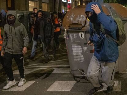 Un encapuchado arrastra un contenedor en Barcelona.