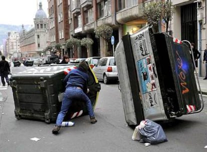 Un encapuchado se oculta tras un contenedor volcado en una calle de Bilbao tras la manifestación.