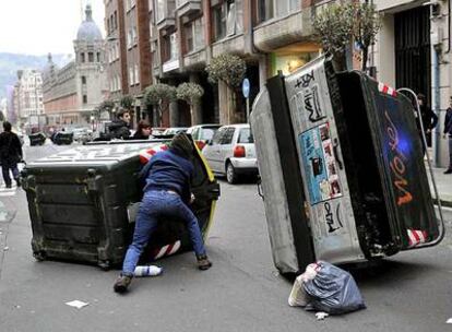 Un encapuchado se oculta tras un contenedor volcado en una calle de Bilbao tras la manifestación.