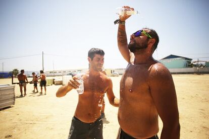 Dos operarios, que trabajan en el desmontaje de los escenarios del festival Cabo de la Plata, se refrescan con agua, en Barbate, Cádiz.