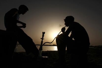 Homens fumam um cachimbo perto do mar em Benghazi (Líbia).