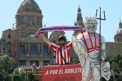 Un aficionado del Atlético exhibe una bufanda de su equipo en la 'fan zone' de Montjuic junto a una réplica de Neptuno.