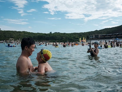 Uma criança com uma touca de natação com a bandeira da China é vista com o pai, na praia de Dongchong.