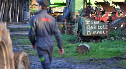 Uno de los residentes de Notre-Dame-des-Landes camina entre maquinaria agrícola. Escrito con pintura el letrero "Zona Agrícola Durable".