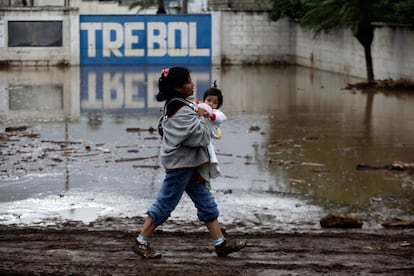 Un mujer, con un niño en los brazos, camina por las calles anegadas de Amatitilian, Guatemala.