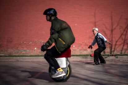 Un hombre practica ejercicios con una espada mientras otro hombre con un monociclo, en Pekín (China).