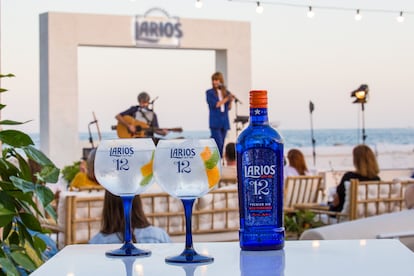 Una botella de la ginebra Premium Larios 12. Al fondo, La Bien Querida durante su conciertos en los Atardeceres Larios.