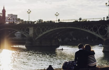 Una pareja se besa en la orilla del río Guadalquivir frente al puente de Triana (Sevilla).