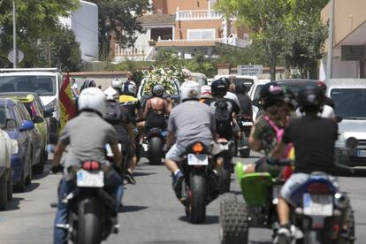Varias personas en moto siguen al coche fúnebre.