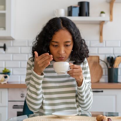 African-american female having long-term covid effect. Concept of loosing sense of smell. Lack of coffee flavor. Coronavirus symptoms. Sitting in white kitchen. Dealing with long-lasting blindness