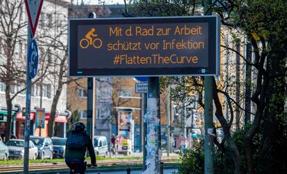 Un ciclista pasea junto a un cartel en Berlín en el que se anima a utilizar la bicicleta para aplanar la curva del coronavirus.