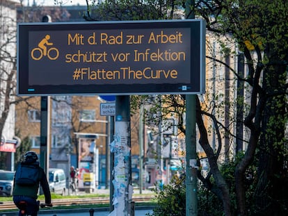 Un ciclista pasea junto a un cartel en Berlín en el que se anima a utilizar la bicicleta para aplanar la curva del coronavirus.