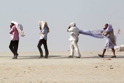 Unos hombres cubren sus caras mientras se abren paso en la orilla del río Ganges durante una tormenta de polvo en Allahabad (India)