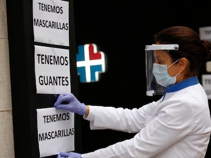 Una farmacéutica de Terrassa (Barcelona) coloca carteles para anunciar que en la farmacia venden mascarillas y guantes, el pasado jueves.