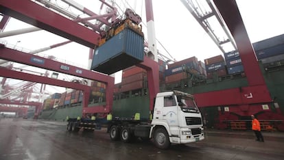 Un operario observa las labores de carga de un contenedor en un cami&oacute;n en un puerto. 